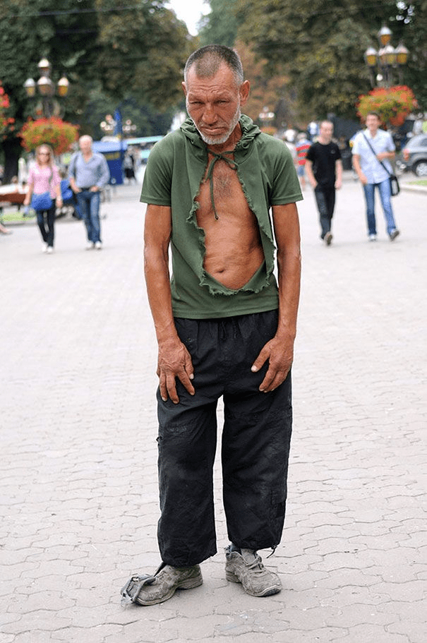 eec47823e941cb2d19dc4f0a5e5dc48a A homeless man standing in public with a ripped shirt on