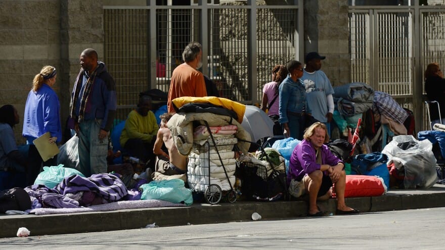 A group of homeless people sitting on the sidewalk.